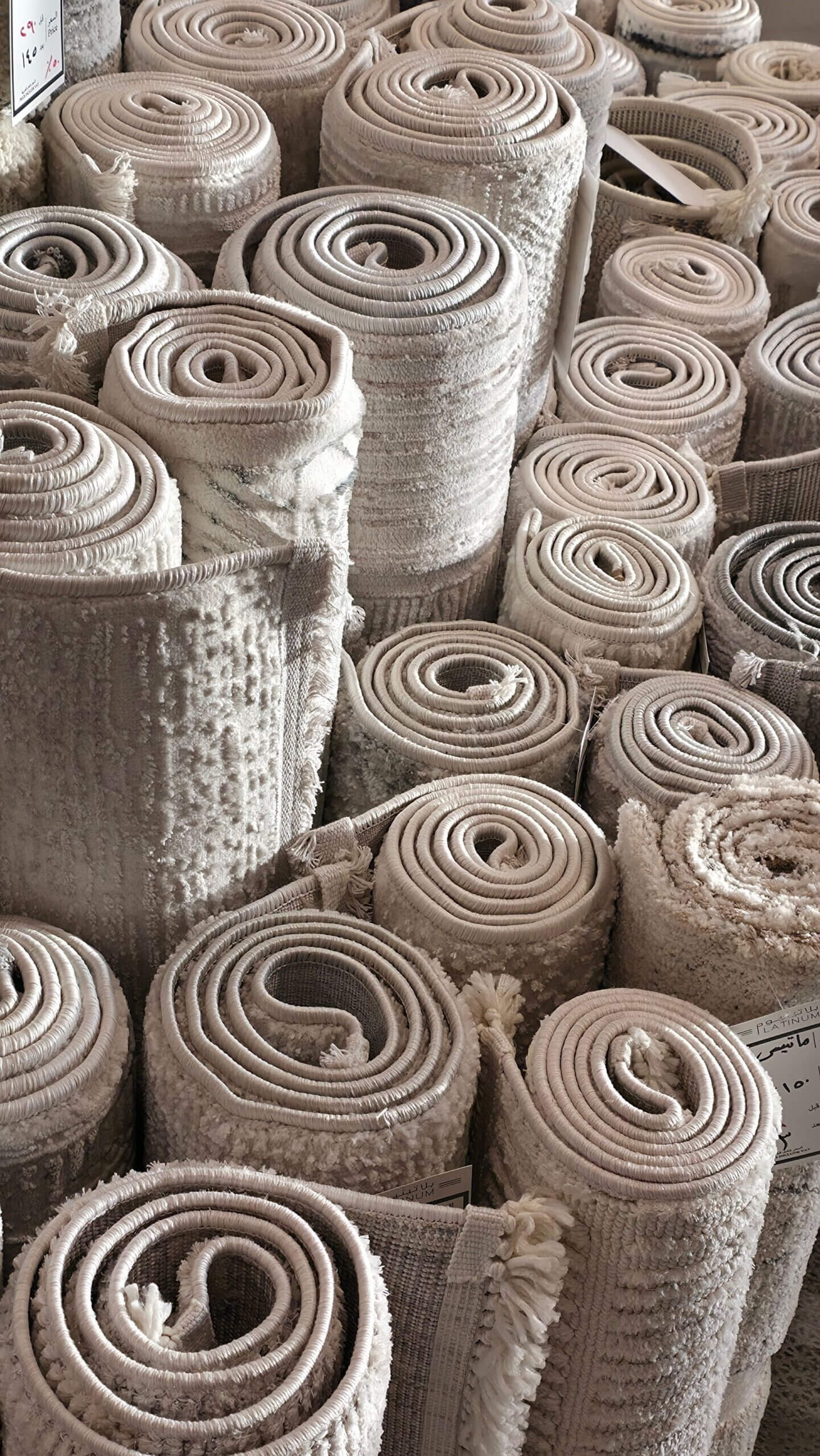 ANASAYFA Elegant rolled carpets neatly stacked in a Jeddah market, showcasing intricate textures and neutral tones.